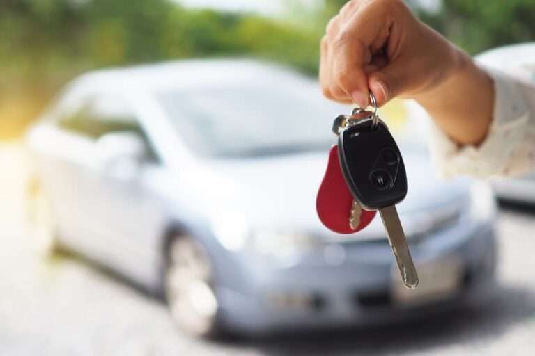 personne tenant des clefs de voiture en premier plan et une voiture garée en arrière plan